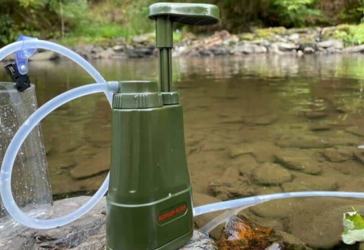 Groen waterfilter met transparante slang en opvangzak bij een ondiepe beek