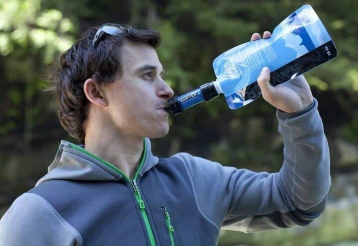 Wandelaar drinkt uit een waterfilterfles in een bosrijke omgeving