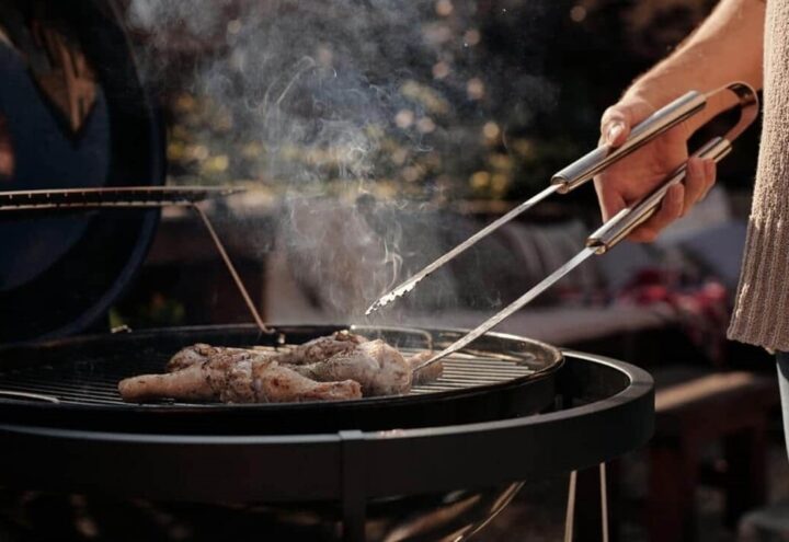 Kip op een ronde barbecue terwijl iemand het vlees met een tang omdraait