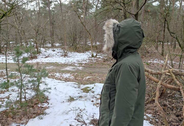 Persoon in donkergroene winterparka met bontkraag in een besneeuwd bos