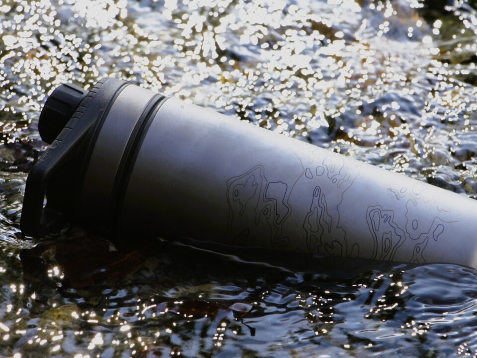 Review: Grayl GeoPress Ti waterfilter & purifier 1 Grijze waterfilterfles met zwarte dop in een ondiepe, kabbelende beek