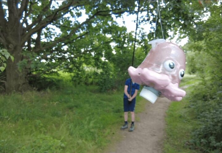 Wandelaar onder een hangende roze visvormige hengelcache op een bospad