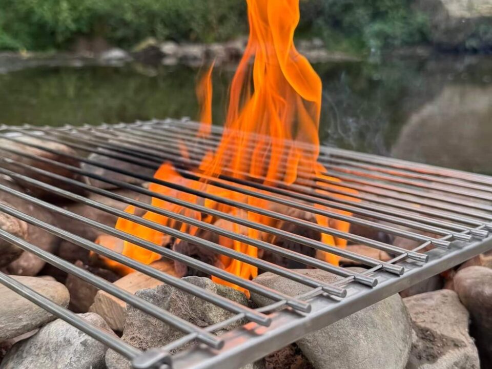Review: Grill van By Arnaud – Voor wie écht wil koken op vuur 1 Metalen grillrooster boven een open vuur tussen stenen aan de rand van het water