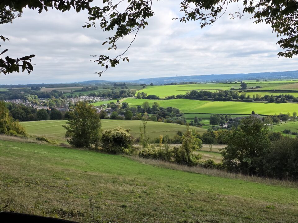 Solo de Dutch Mountain Trail: vier dagen door Limburg 1 Uitzicht over groene velden, een dorp en beboste heuvels onder een bewolkte lucht