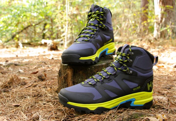 Twee donkerblauwe halfhoge wandelschoenen met felgele accenten op een boomstronk in het bos