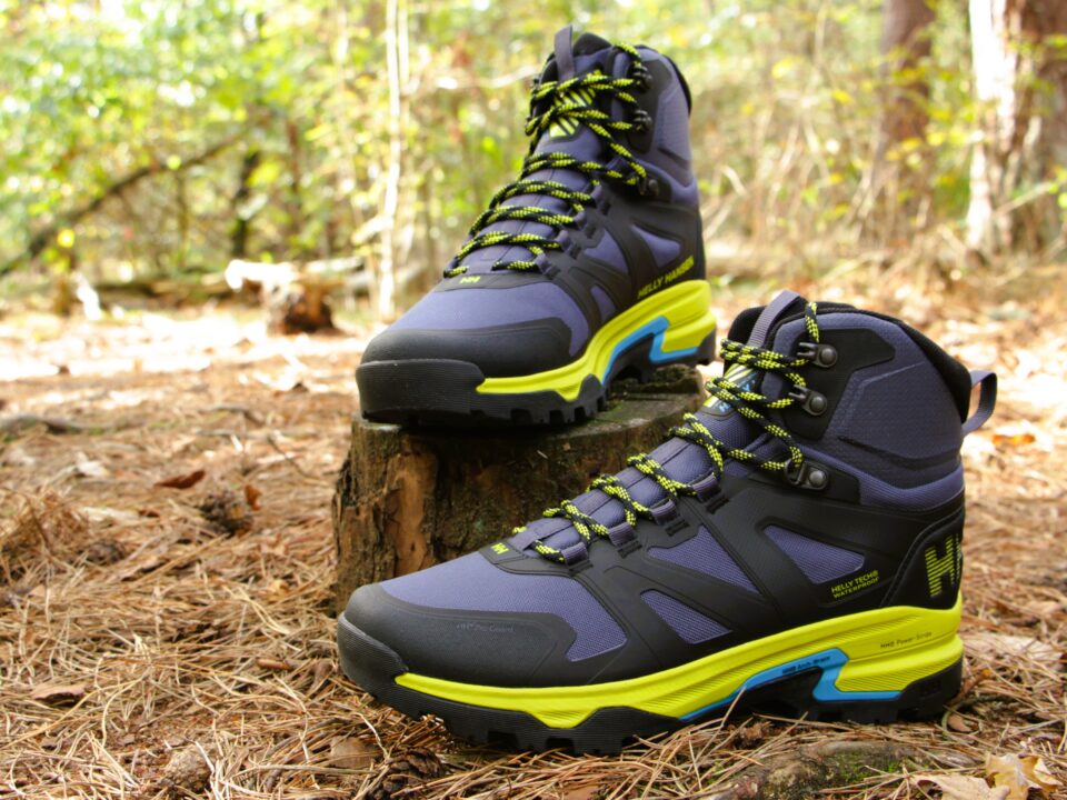 Review Helly Hansen Ascender Mid HT 1 Twee donkerblauwe halfhoge wandelschoenen met felgele accenten op een boomstronk in het bos