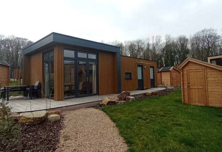 Houten vakantiehuisjes rond een modern chalet met terras, grindpad en grasveld