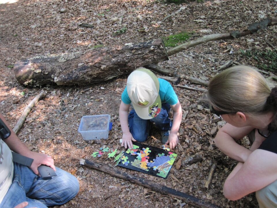 Geocaching met kinderen: schatzoeken in het wild 1 Kinderen leggen een kleurrijke puzzel op de bosgrond naast een omgevallen boom