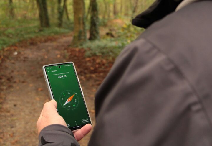 Wandelaar houdt een smartphone met kompasapp boven een bospad