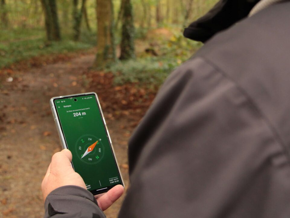 Wandelaar houdt een smartphone met kompasapp boven een bospad