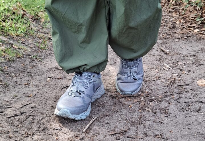 Grijze wandelschoenen onder een groene wandelbroek op een onverhard bospad