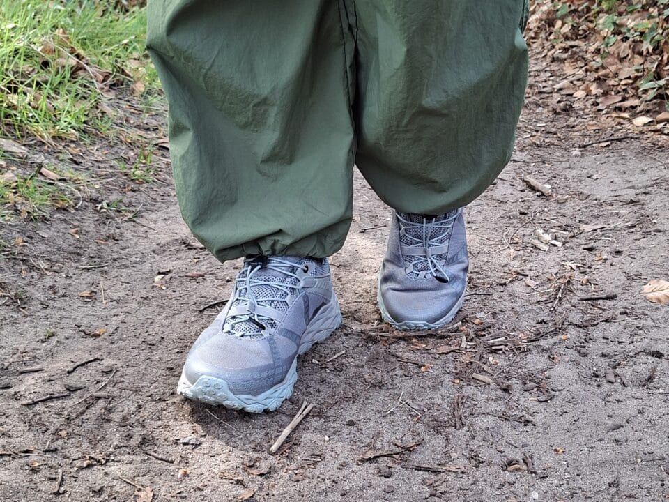 Grijze wandelschoenen onder een groene wandelbroek op een onverhard bospad