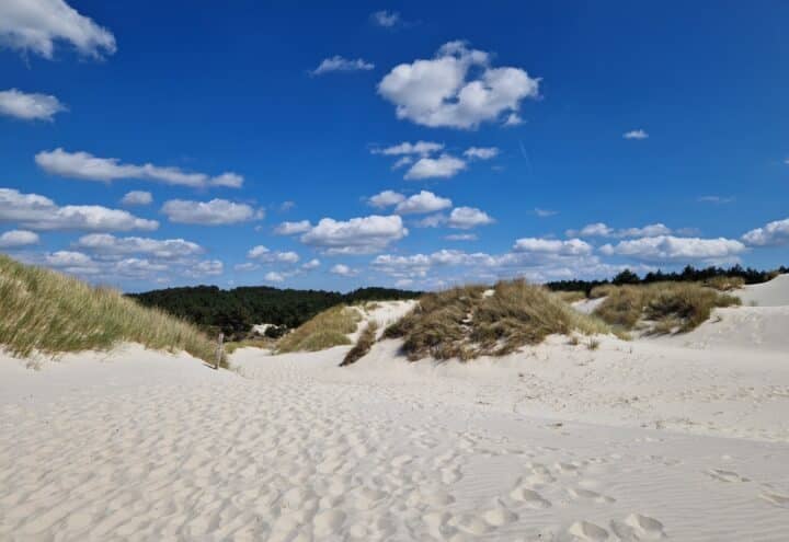 Zandpad tussen witte duinen met helmgras onder een blauwe lucht met wolken