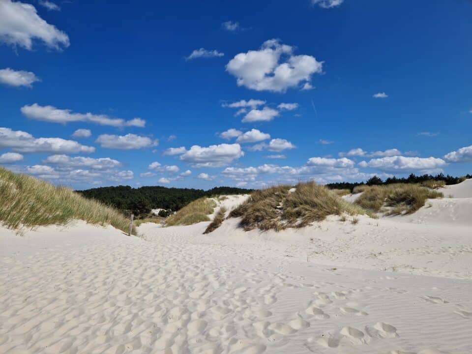 Zandpad tussen witte duinen met helmgras onder een blauwe lucht met wolken