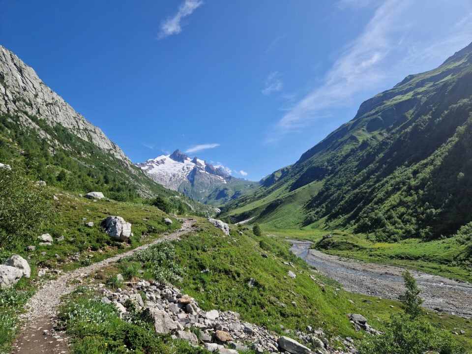 Tour du Mont Blanc ervaringen: hoe het echt was 1 Bergdal met een rotsachtig wandelpad, groene hellingen en besneeuwde bergtoppen onder een blauwe lucht