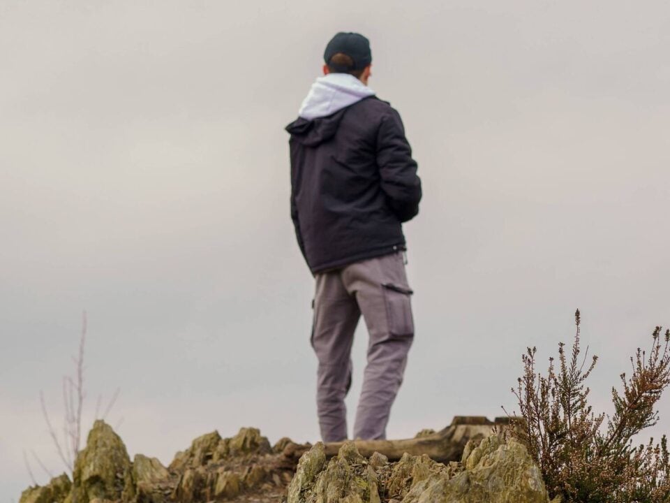 Wat is een softshell jas, en wanneer kies je een hardshell? 1 Wandelaar in donkere jas staat op een rotsachtige heuvel onder een bewolkte lucht
