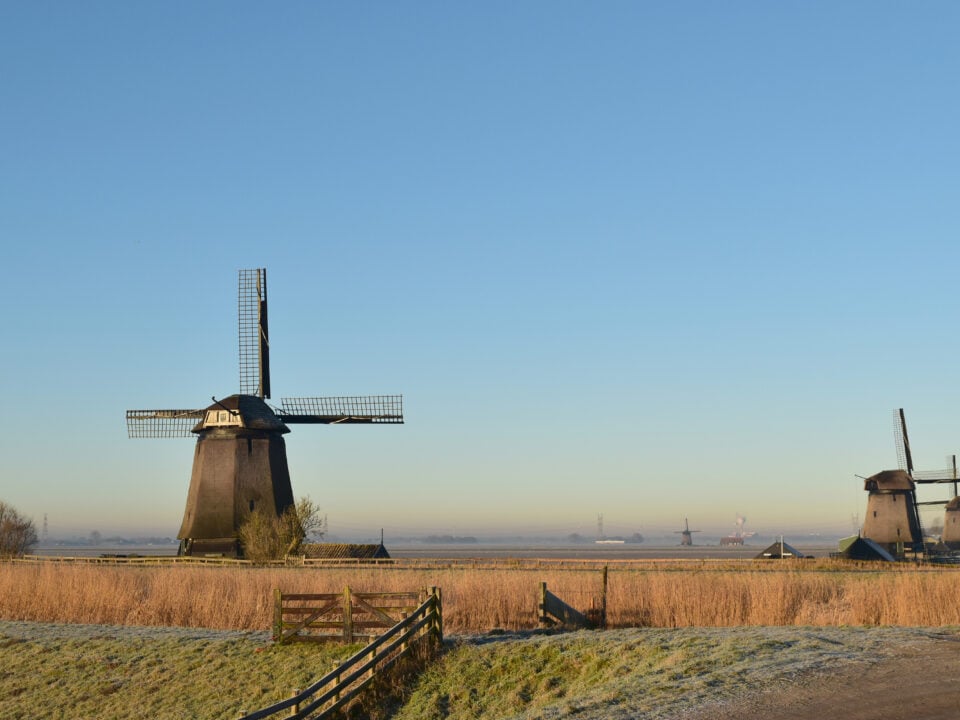 Wandelen in de Eilandspolder: op pad vanuit De Rijp 1 Drie windmolens in een bevroren polderlandschap met een houten hek op de voorgrond