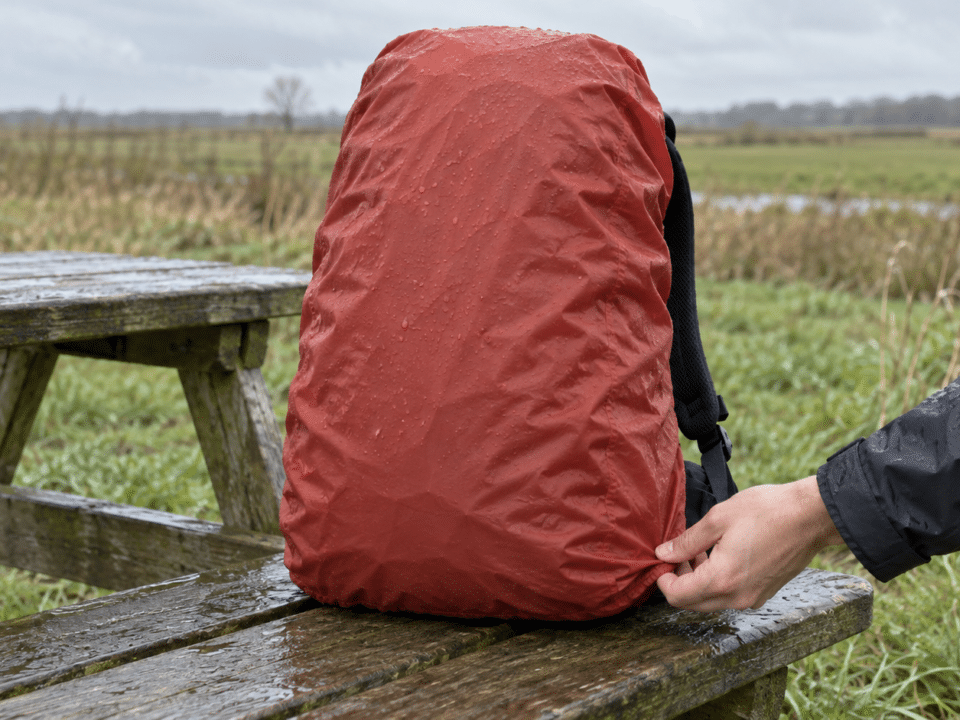 Rode regenhoes om een rugzak op een natte houten picknickbank