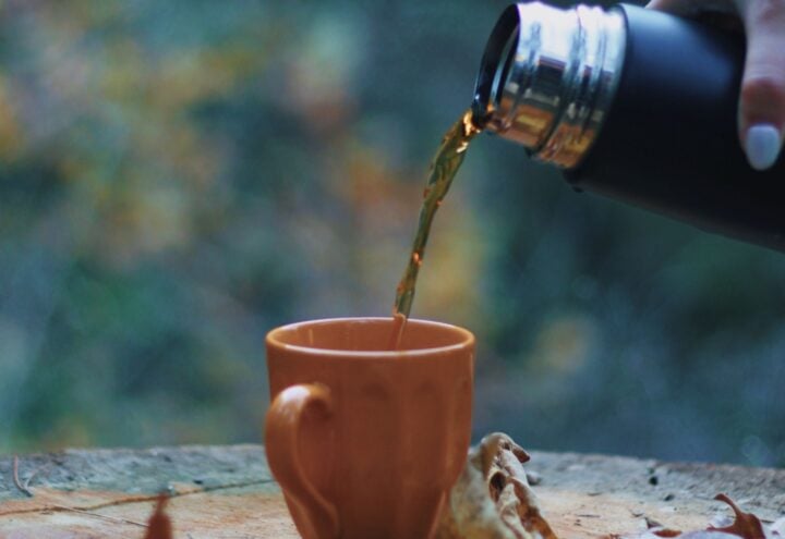 Warme drank wordt vanuit een thermosfles in een oranje mok geschonken