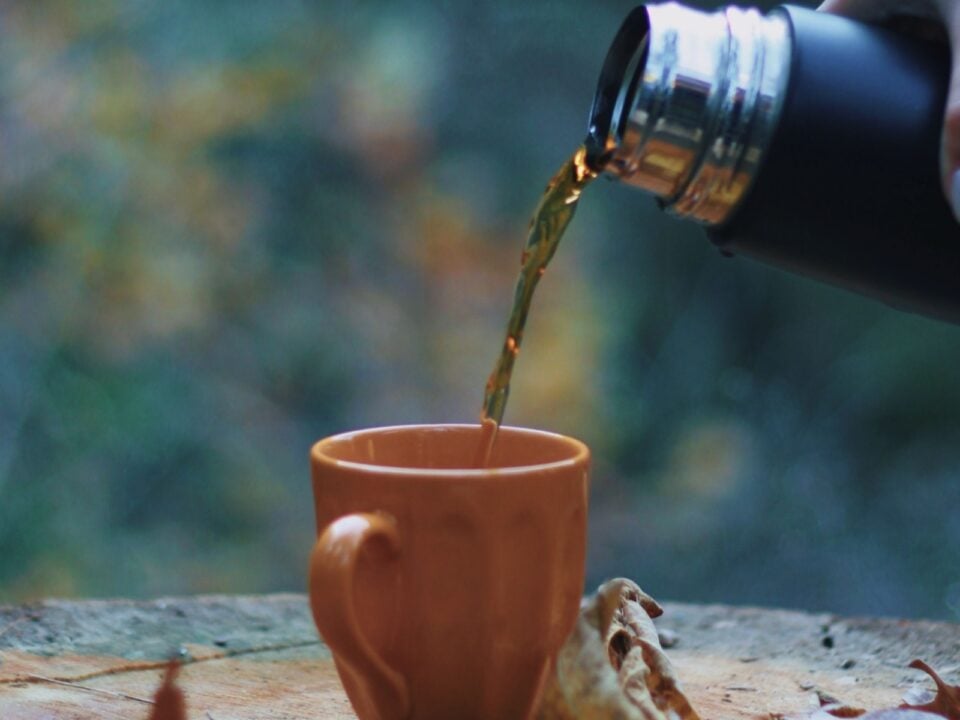Warme drank wordt vanuit een thermosfles in een oranje mok geschonken