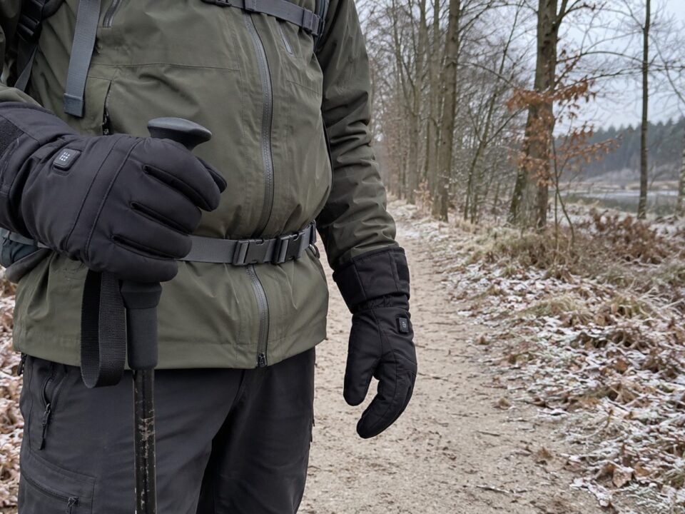 Wandelaar met zwarte verwarmde handschoenen op een besneeuwd bospad
