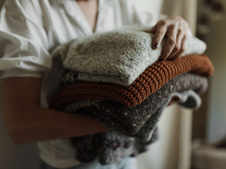 Persoon houdt een stapel opgevouwen gebreide kleding vast