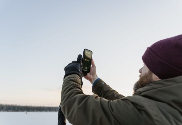 Man met muts gebruikt een smartphone bij een besneeuwd landschap